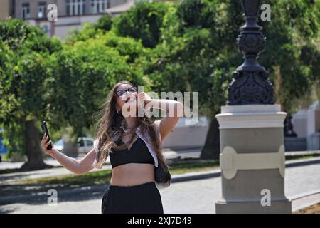 Nicht exklusiv: ODESA, UKRAINE - 13. JULI 2024 - Eine lächelnde Frau hält ein Smartphone an einem heißen Sommertag in Odesa, Südukraine. Stockfoto