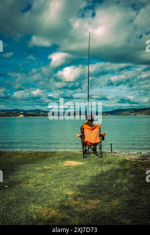 Ohope New Zealand - 26. Mai 2012; einsamer fischer sitzt im Klappstuhl und hält eine Angelrute am Ufer des Hafens von Ohiwa; Stockfoto