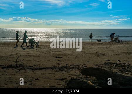 Whakatane Neuseeland - 26. Mai 2012; Licht am späten Nachmittag mit Silhouettenfiguren am Strand in sade und hellblauem Himmel über dem Horizont. Stockfoto