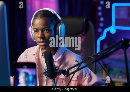 Porträt der jungen schwarzen Frau als weibliche Gamerin, die Online-Stream im Studio mit rosa Neonlichtern aufnimmt Stockfoto