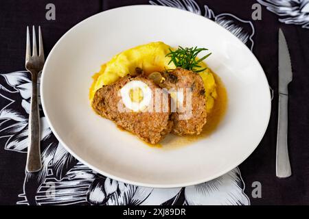 Gebackenes Schweinefleisch- und Rindfleischpüree mit Ei, Kartoffelpüree und Rosmarinzweig auf weißem Teller auf tiefblauem Tischtuch, Nahaufnahme. Stockfoto