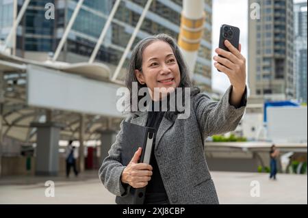Eine selbstbewusste, attraktive asiatische Geschäftsfrau in einem formellen Business-Anzug nimmt Selfies mit ihrem Smartphone auf, während sie zur Arbeit pendelt und mich steht Stockfoto