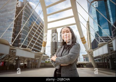 Eine selbstbewusste, reife asiatische Geschäftsfrau oder Geschäftsführerin in einem formellen Business-Anzug steht mit überkreuzten Armen in der großen Stadt und lächelt das Kommen an Stockfoto