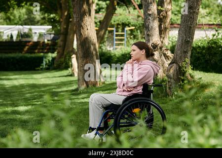 Eine junge Frau sitzt im Rollstuhl und blickt nachdenklich auf einen üppig grünen Park. Stockfoto