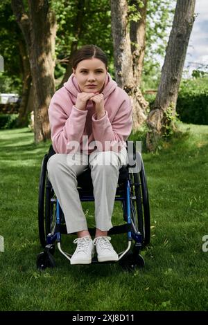 Eine junge Frau in einem rosa Hoodie sitzt in einem Rollstuhl in einem grasbewachsenen Park. Stockfoto