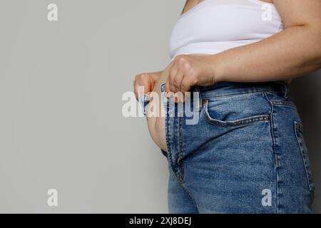 Weibliche Person, die versucht, ihre Jeanshosen auf weißem Hintergrund zu ziehen, Diätkonzept Stockfoto