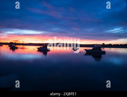 Intensive Sonnenuntergangsfarben und Reflexionen bei langer Exposition mit leicht verschwommenen Booten in der Bucht von Whakatane Harbour. Stockfoto