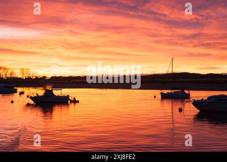 Intensiver Sonnenuntergang in Rosa, Rot und Orange spiegelt sich auf dem Wasser der Bucht des Hafens Whakatane und über den festgefahrenen Booten in Silhouette Stockfoto