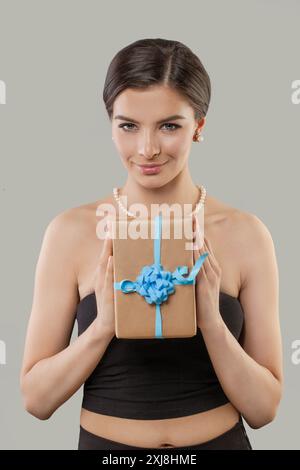 Hübsche junge Frau, die Geschenkbox mit blauem Band hält und in die Kamera schaut Stockfoto