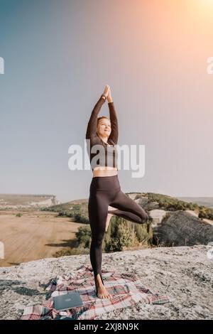 Frau, die Yoga auf dem Berggipfel mit Laptop übt Stockfoto