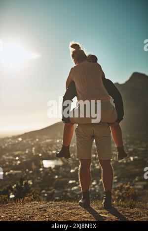 Huckepack, Paare und Abenteuer auf den Bergen zum Wandern, Liebe und Sonnenuntergang mit der Stadtlandschaft. Mann, Frau und zusammen in der Natur zum Trekking, Reisen und Stockfoto