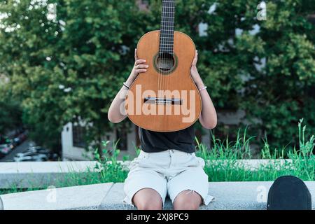 latina-Frau bedeckt ihr Gesicht mit einer elektrischen Gitarre Stockfoto