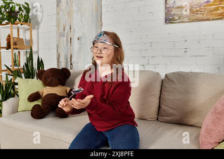 Ein kleines Mädchen mit Down-Syndrom trägt eine Krone und spielt zu Hause mit einem Spielzeug. Stockfoto