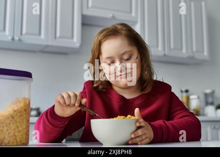 Ein kleines Mädchen mit Down-Syndrom genießt eine Schüssel Müsli in ihrer Küche. Stockfoto