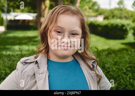 Ein kleines Mädchen mit Down-Syndrom lächelt hell, während es draußen ist. Stockfoto