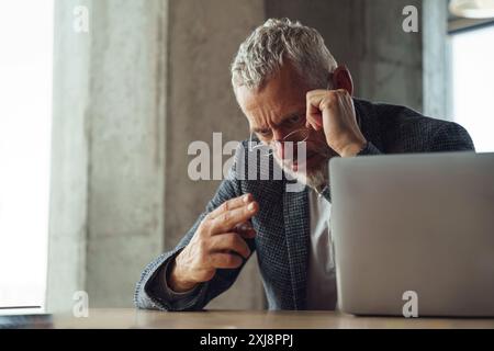 Ein Mann sitzt an einem Schreibtisch und konzentriert sich auf einen Laptop vor ihm Stockfoto