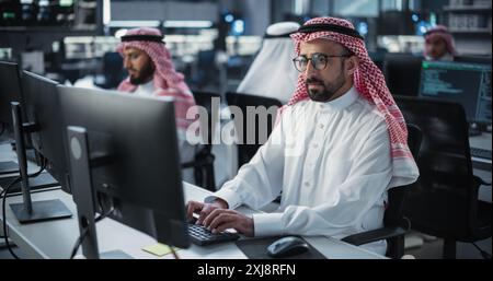 Porträt eines intelligenten Programmierers aus dem Nahen Osten, der in einem technologischen Unternehmensbüro am Computer arbeitet. Young Gulf man entwickelt Software für ein generatives KI-Projekt Stockfoto
