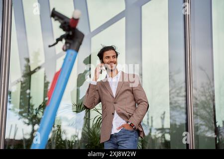 Geschäftsmann, der mit seinem Smartphone in einem Bürogebäude mit einem Elektroroller spricht Stockfoto