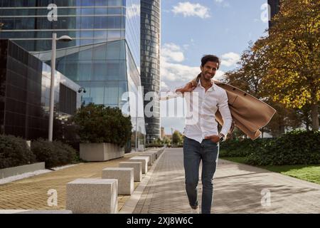 Junger indischer Modemann in eleganten Kleidern trägt seinen Blazer in der Hand und legt ihn auf die Schulter Stockfoto