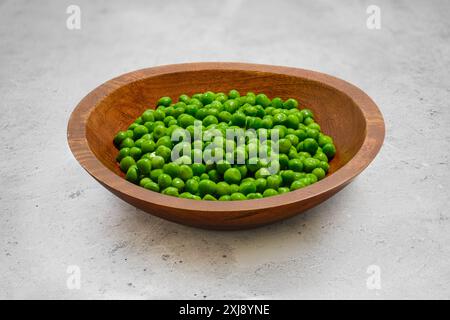 Frische grüne Erbsen in einer Holzschale auf einem grauen Steintisch aufgetaut Stockfoto