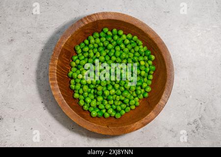 Blick von oben auf aufgetaute frische grüne Erbsen in einer Holzschale auf einem grauen Steintisch Stockfoto