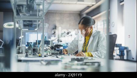 Junge afrikanische Wissenschaftsstudentin, die Elektronikexperimente in einem Universitätsworkshop durchführt. Diverse Schwarze Gelehrte mit Mikroskop, die an der Verbindung und Prüfung einer Leiterplatte in einem Labor arbeiten Stockfoto