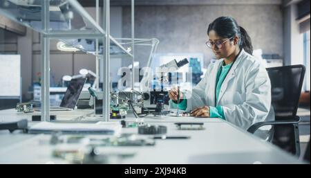 Junger indischer Wissenschaftsstudent, der Elektronikexperimente in einem Universitätsworkshop durchführt. Verschiedene junge Gelehrte mit Mikroskop, die an der Verbindung einer Leiterplatte arbeiten Stockfoto