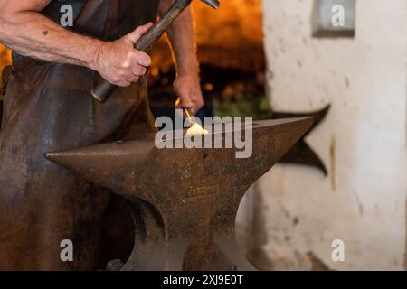 Varberg, Schweden - 4. Juli 2022: Schmied hämmert auf rotem heißem Eisen auf einem großen Amboss. Stockfoto