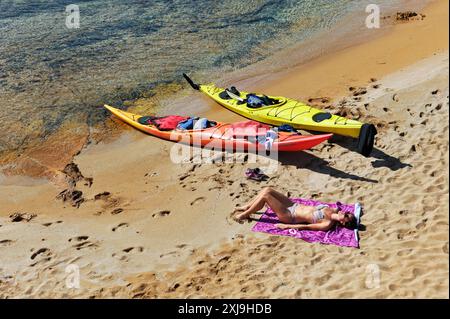 Kajakfahrer, der sich am Strand einer Insel in der Bucht Cala Pregonda in der Nähe von Kap Cavalleria an der Nordküste von Menorca, Balearen, Spanien, ausruhen lässt. Stockfoto