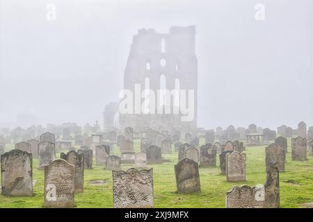 Ein nebeliger Friedhof mit alten Grabsteinen und einem großen, alten, ruinierten Gebäude im Hintergrund, Großbritannien, Europa Copyright: VasilexJechiu 1385-354 Stockfoto