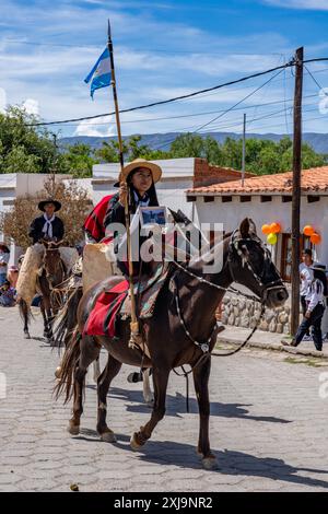 Ein weiblicher Gaucho, der einen traditionellen roten Salteño Poncho trägt, reitet bei einer Parade in Cachi, Argentinien. Traditionell als "china" bezeichnet, was ein ist Stockfoto