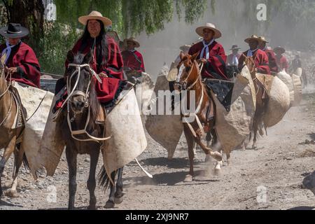 Ein weiblicher Gaucho im traditionellen roten Salteño Poncho reitet an der Spitze einer Gruppe von Gauchos in Cachi, Argentinien. Ein weiblicher Gaucho wurde traditionell genannt Stockfoto