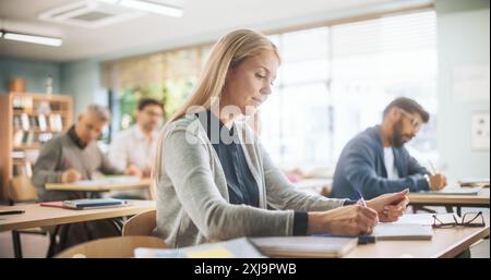 Verschiedene Gruppe multiethnischer junger und älterer Erwachsener, die im Auditorium sitzen und an einer Lehrvorlesung zur Verbesserung der beruflichen Arbeitsfähigkeiten teilnehmen. Frauen mittleren Alters, die sich auf anstehende Prüfungen vorbereiten Stockfoto
