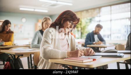 Porträt einer glücklichen Seniorin, die einen Kurs in einem Internationalen Erwachsenenbildungszentrum macht. Ältere Frauen tragen eine Brille, sitzen hinter einem Schreibtisch und schreiben Notizen in Notizbuch Stockfoto