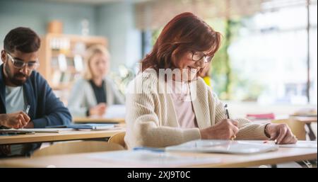 Porträt einer glücklichen Seniorin, die einen Kurs in einem Internationalen Erwachsenenbildungszentrum macht. Alte Frau trägt eine Brille, sitzt hinter einem Schreibtisch, benutzt Lehrbuch und schreibt Notizen in Notizbuch Stockfoto