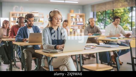 Verschiedene ältere Schüler lernen im Unterricht, sitzen hinter Schreibtischen mit Kopfhörern, verwenden Laptops und schreiben in Notebooks. Lehrer, der einen Kurs zur Erwachsenenbildung per Fernzugriff online abhält Stockfoto