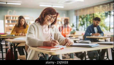 Porträt einer glücklichen Seniorin, die einen Kurs in einem Internationalen Erwachsenenbildungszentrum macht. Fokussierte ältere Frauen, die eine Brille tragen, hinter einem Schreibtisch sitzen und Notizen in ein Notizbuch schreiben. Stockfoto