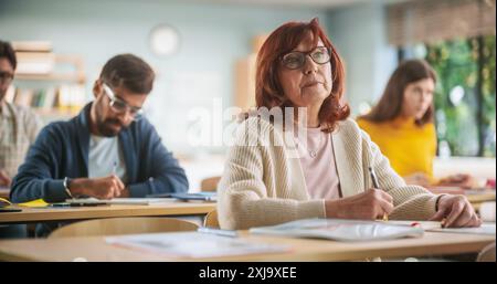 Porträt einer glücklichen Seniorin, die einen Kurs in einem Internationalen Erwachsenenbildungszentrum macht. Alte Frau trägt eine Brille, sitzt hinter einem Schreibtisch, benutzt Lehrbuch und schreibt Notizen in Notizbuch Stockfoto