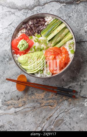 Sushi-Schüssel mit Lachs, Avocado, Gurke, weißem Reis, Sesam, ginger und Wasabi-Nahaufnahme auf dem Tisch. Vertikale Draufsicht von oben Stockfoto