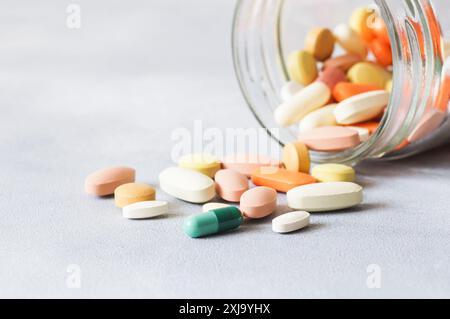 Bunte Tablette, Kapseln, Pillen Medizin verschütten aus Glasflasche auf grauem Hintergrund, Gesundheitswesen und medizinisches Konzept Stockfoto