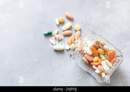 Bunte Tablette, Kapseln, Pillen Medizin verschütten aus Glasflasche auf grauem Hintergrund, Gesundheitswesen und medizinisches Konzept Stockfoto