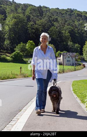 Europa, Luxemburg, Septfontaines, eine ältere Frau, die mit ihrem portugiesischen Wasserhund durch das Eisch-Tal geht Stockfoto