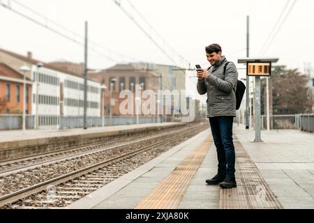 Ein Mann überprüft sein Handy, während er auf einem Bahnsteig steht. Stockfoto