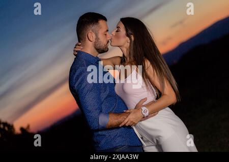 Ein Mann und eine Frau umarmen und küssen sich, während sie auf einem Feld bei Sonnenuntergang stehen. Stockfoto