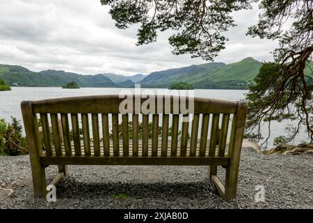 Eine Holzbank befindet sich auf einem Kiesweg mit Blick auf den Derwentwater Lake und die umliegenden Berge im Lake District. Stockfoto
