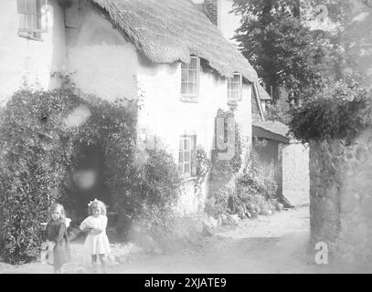 Ein englisches Reetdachhaus mit zwei kleinen Mädchen im Vordergrund, von dem angenommen wird, dass sie sich in Teignmouth, Devon, befinden. Dieses Foto stammt von einem edwardianischen Original, um 1910. Das Original war Teil eines Albums von 150 Albumenfotos von unterschiedlicher Qualität, von denen ich viele fotografiert habe. Die Sammlung enthielt Bilder vor allem von der Isle of man und der englischen Grafschaft Devonshire. Anmerkungen waren im Album enthalten, aber leider gab es keine genauen Daten. Die Originalfotos waren durchschnittlich 6 x 4 ½ Zoll. Stockfoto