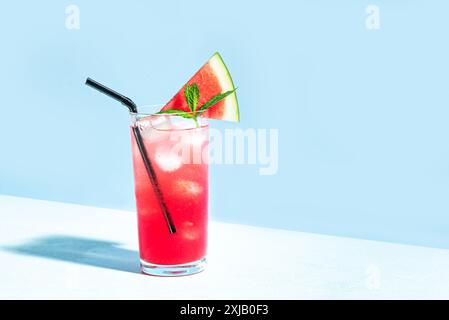 Sommergetränk mit Wassermelone und Minze, kalte Limonade oder Cocktail mit Eis und Wassermelonenscheibe. Trendige Aufnahme mit harten Schatten auf blauem Himmel Hintergrund, Stockfoto