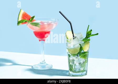 Trendiges Cocktail-Getränk Mojito und rosa Margarita mit Wassermelone, Basilikum und Eis auf hellblauem Hintergrund, Sonnenlicht, Kopierraum. Kreativer Sommer-Cocktai Stockfoto