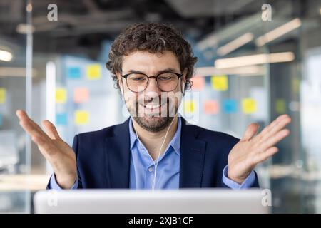 Selbstbewusster Geschäftsmann im Büro, der an virtuellen Besprechungen teilnimmt, lächelt und Gesten gibt, während er Ideen und Strategien diskutiert, Stockfoto