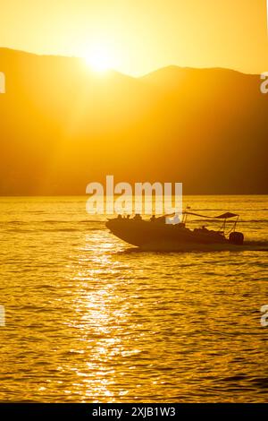 Motorbootfahrt bei Sonnenuntergang. Sommerabend in der Bucht von Kotor, Montenegro: Meereslandschaft mit einem Boot, das durch das goldfarbene Wasser des Meeres segelt Stockfoto